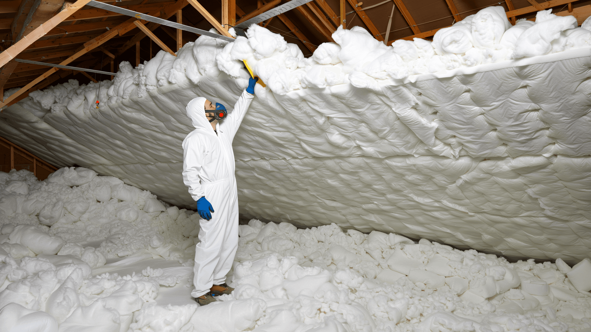 Professional insulation contractor in protective coverall installing blown-in cellulose insulation across a residential attic floor